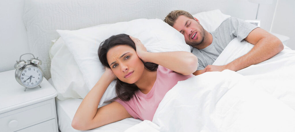 Woman covering her ears while her husband is snoring next to her