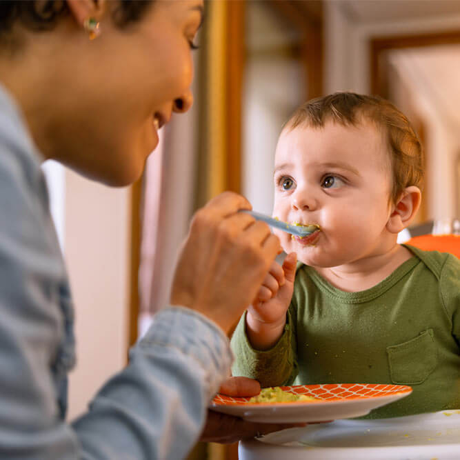 Loving mother spoon-feeding her happy baby boy.