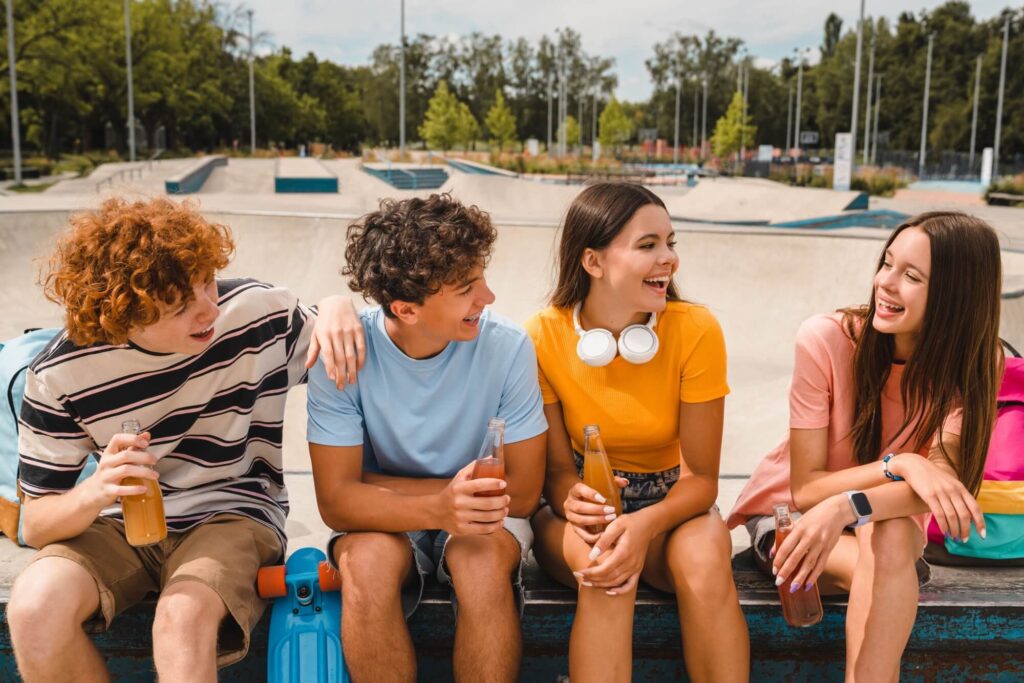 Smiling teenagers friends sitting on ramp skating in skate park