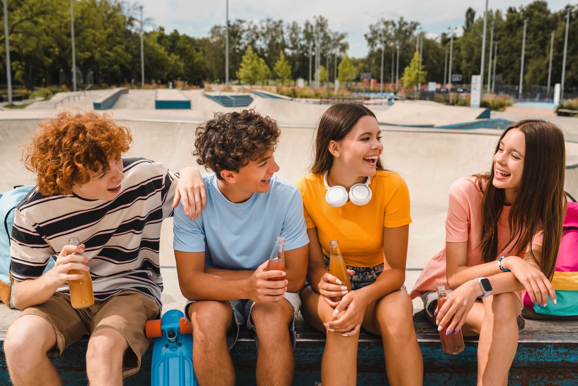 Smiling teenagers friends sitting on ramp skating in skate park