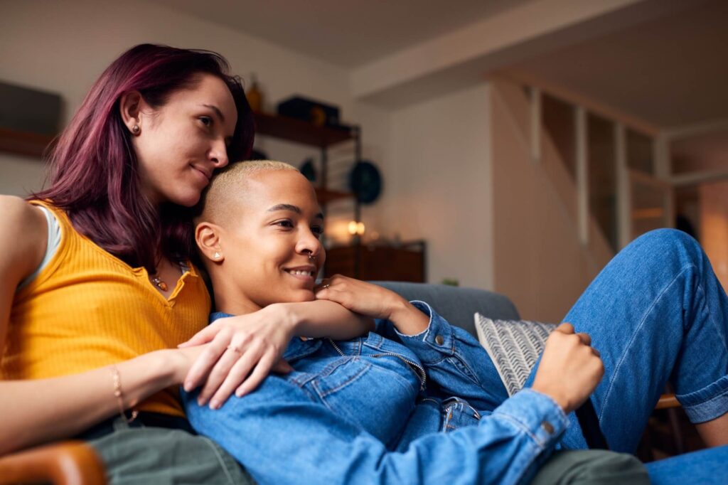 Female friends lying On Sofa At Home Watching