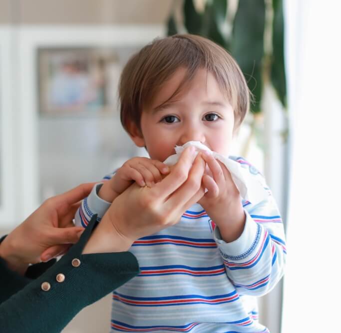 Adorable baby boy blowing nose into tissue paper