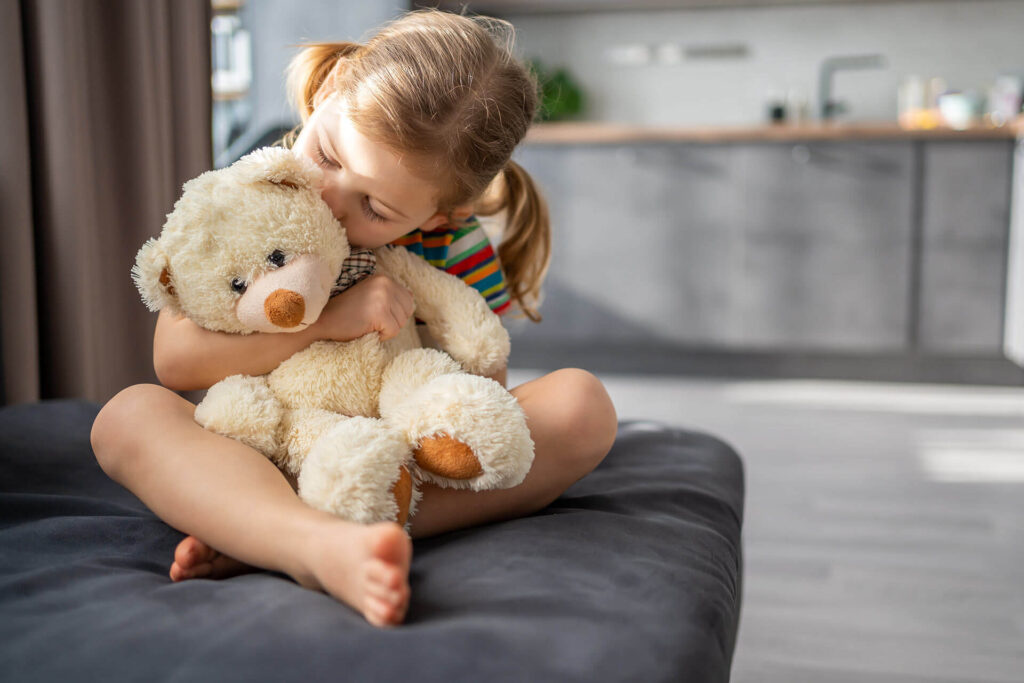 Cute little girl hugging teddy bear while sitting on sofa