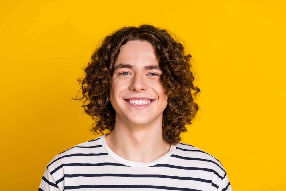 Young curly hair cheerful teenager optimistic boy toothy smile wearing striped t shirt