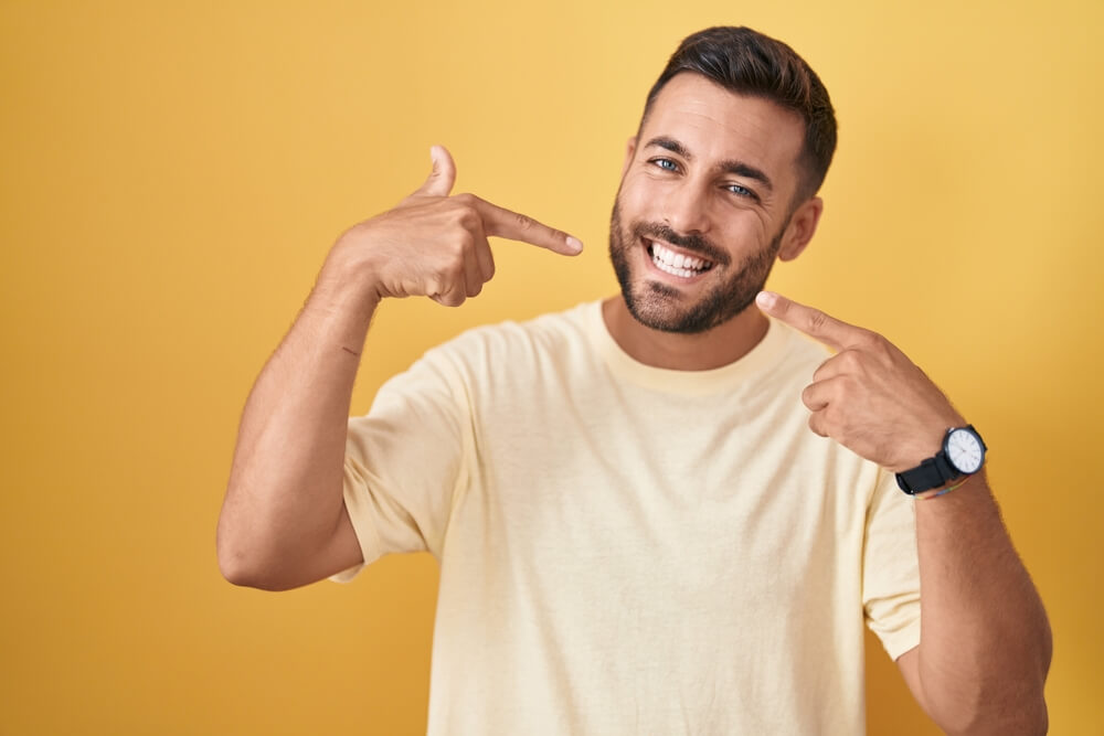 Handsome hispanic man standing over yellow background