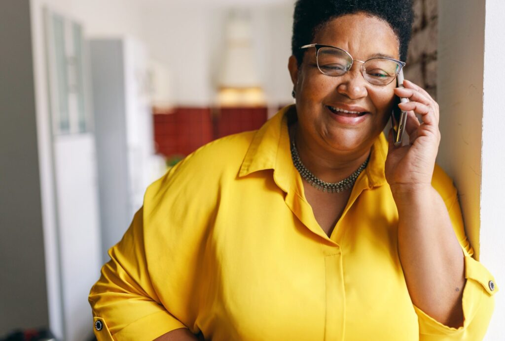 Happy smiling senior female in yellow shirt and glasses having conversation on phone
