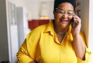 Happy smiling senior female in yellow shirt and glasses having conversation on phone
