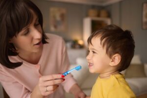 Mother teaching and helping her son brush his teeth at home