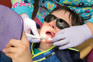 Teenage boy with Autism and Down's Syndrome holds a mirror as he is taught proper dental hygiene and brushing