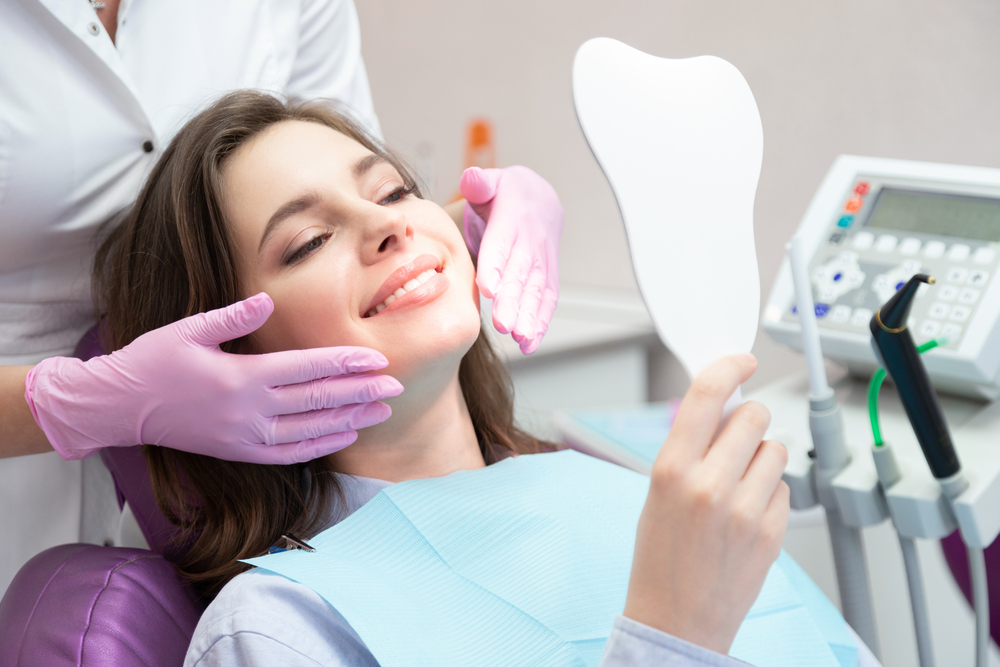 Smiling woman after teeth whitening procedure looking at mirror, caries treatment