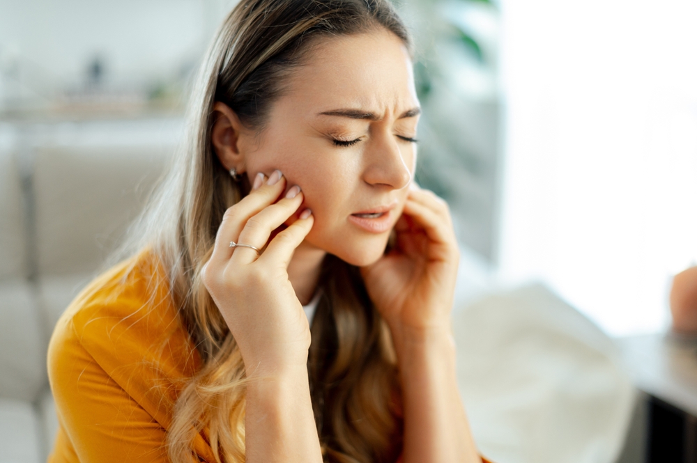 Tooth pain concept. Caucasian young woman in a yellow shirt sits on a couch at home