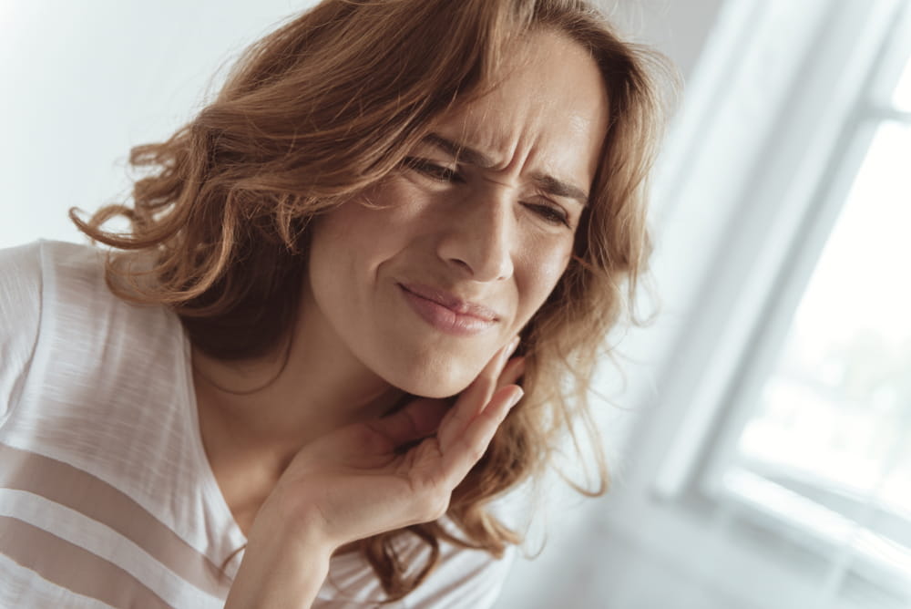 Need to call my doctor. Portrait of a stressed woman pressing her cheek while struggling with a strong toothache indoors.