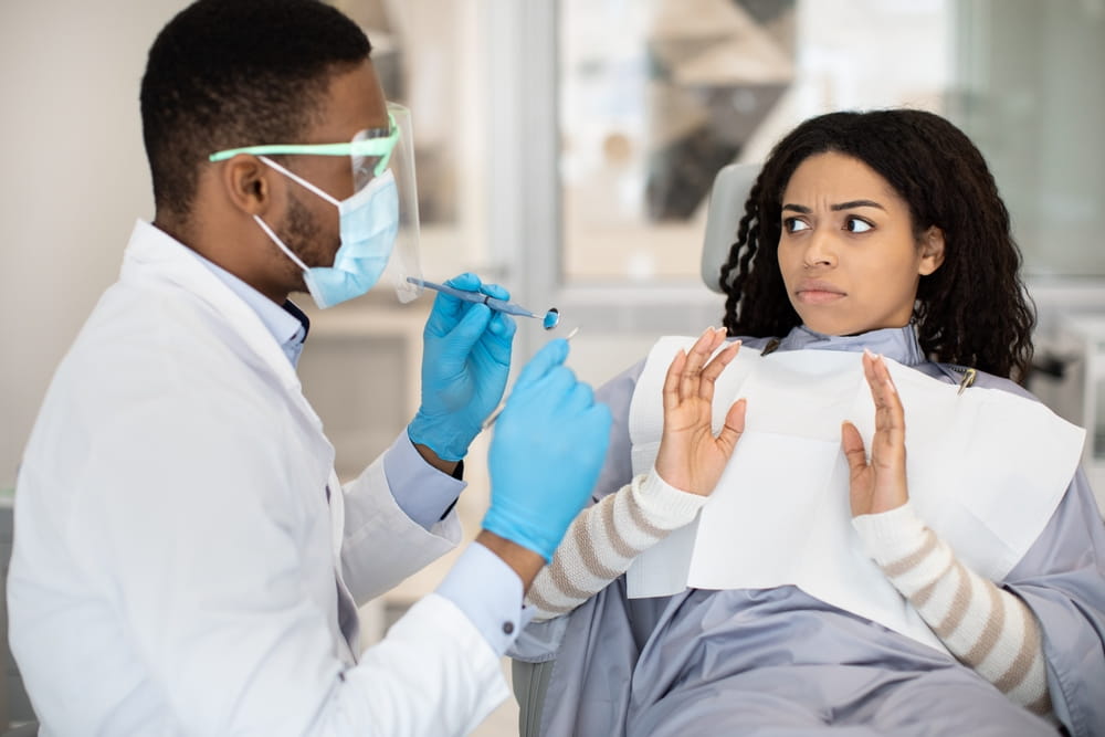 Worried Black Female Patient Looking At Dentist Doctor With Shock During Check Up In Clinic