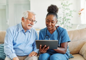 Doctor or nurse caregiver showing a tablet screen to senior man and laughing at home or nursing home