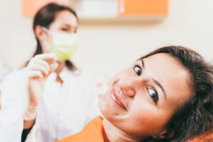 Young dentist holding a tooth and smiling patient in dentist office. Focus on the patient