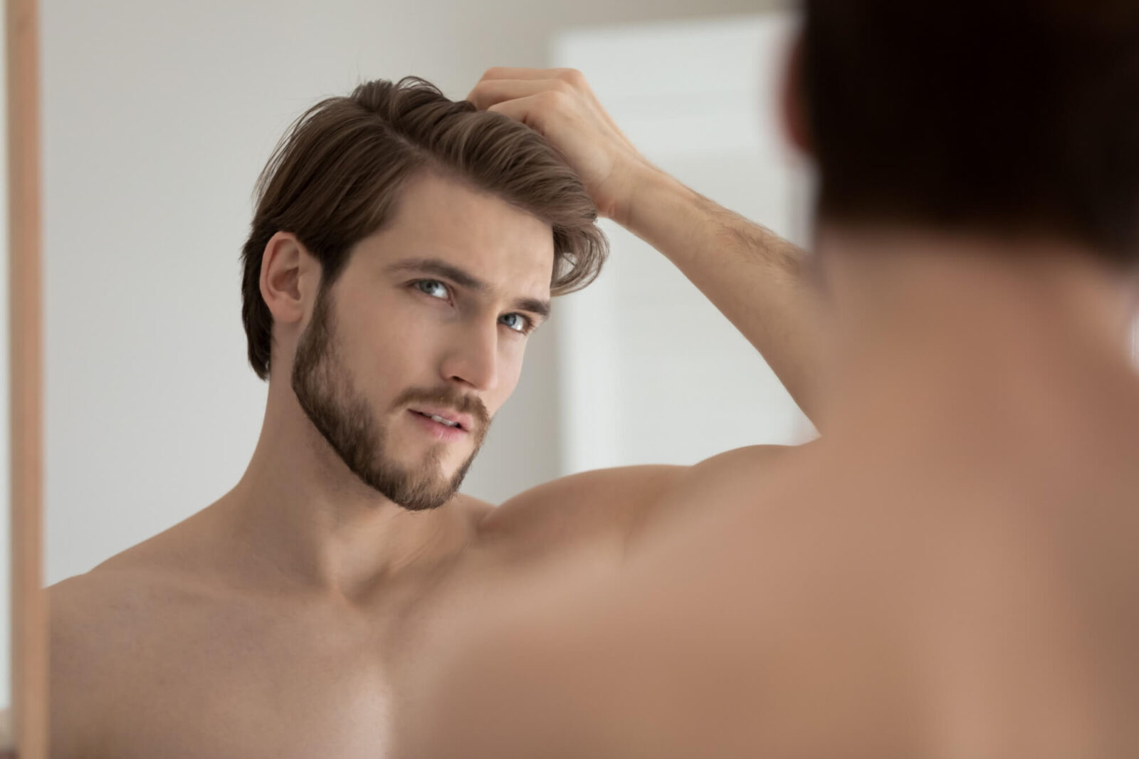 Young shirtless guy looks in mirror touch hair