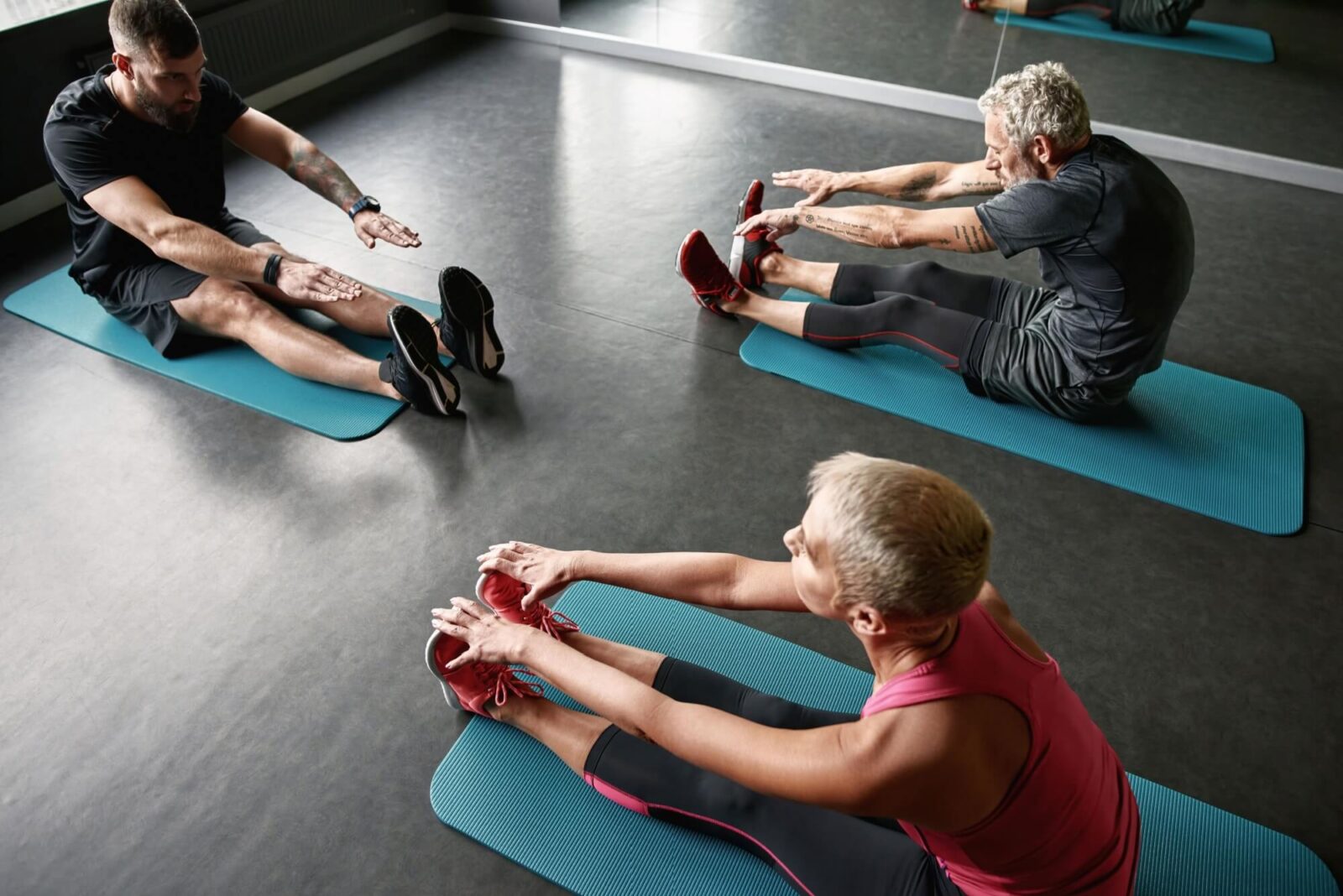 sports people of different age stretching on dark gym floor