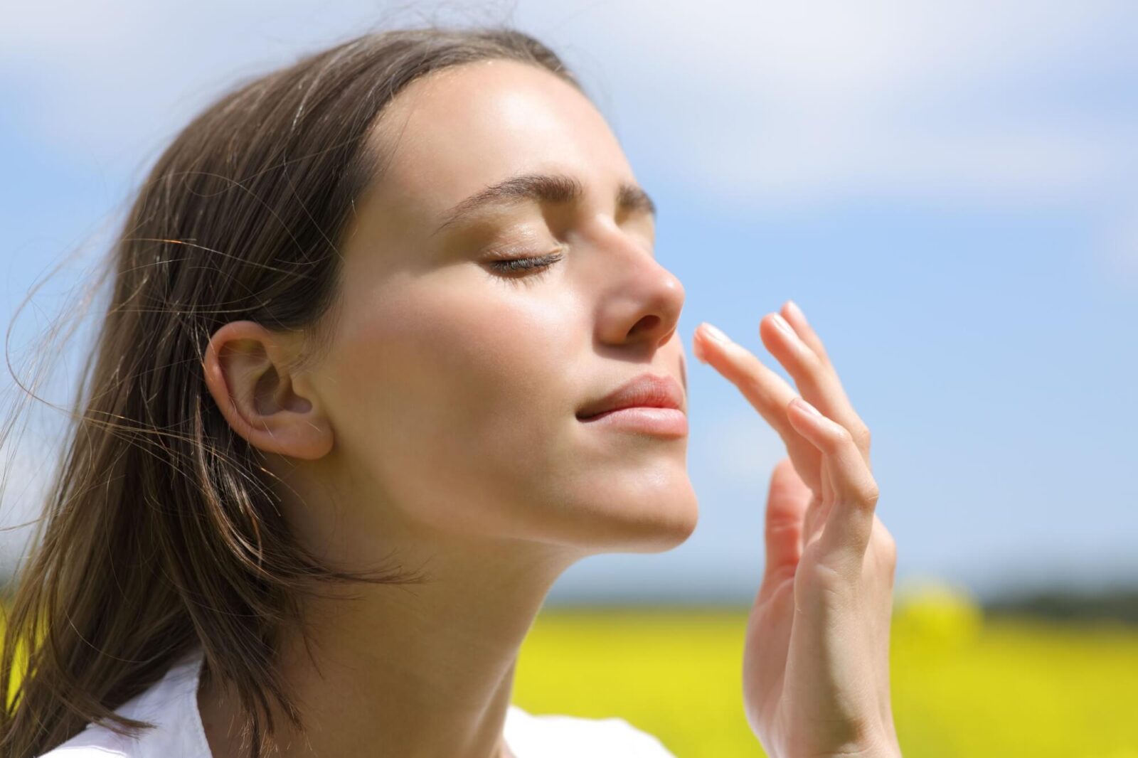 beautiful woman putting moisturizer cream on cheek in a field