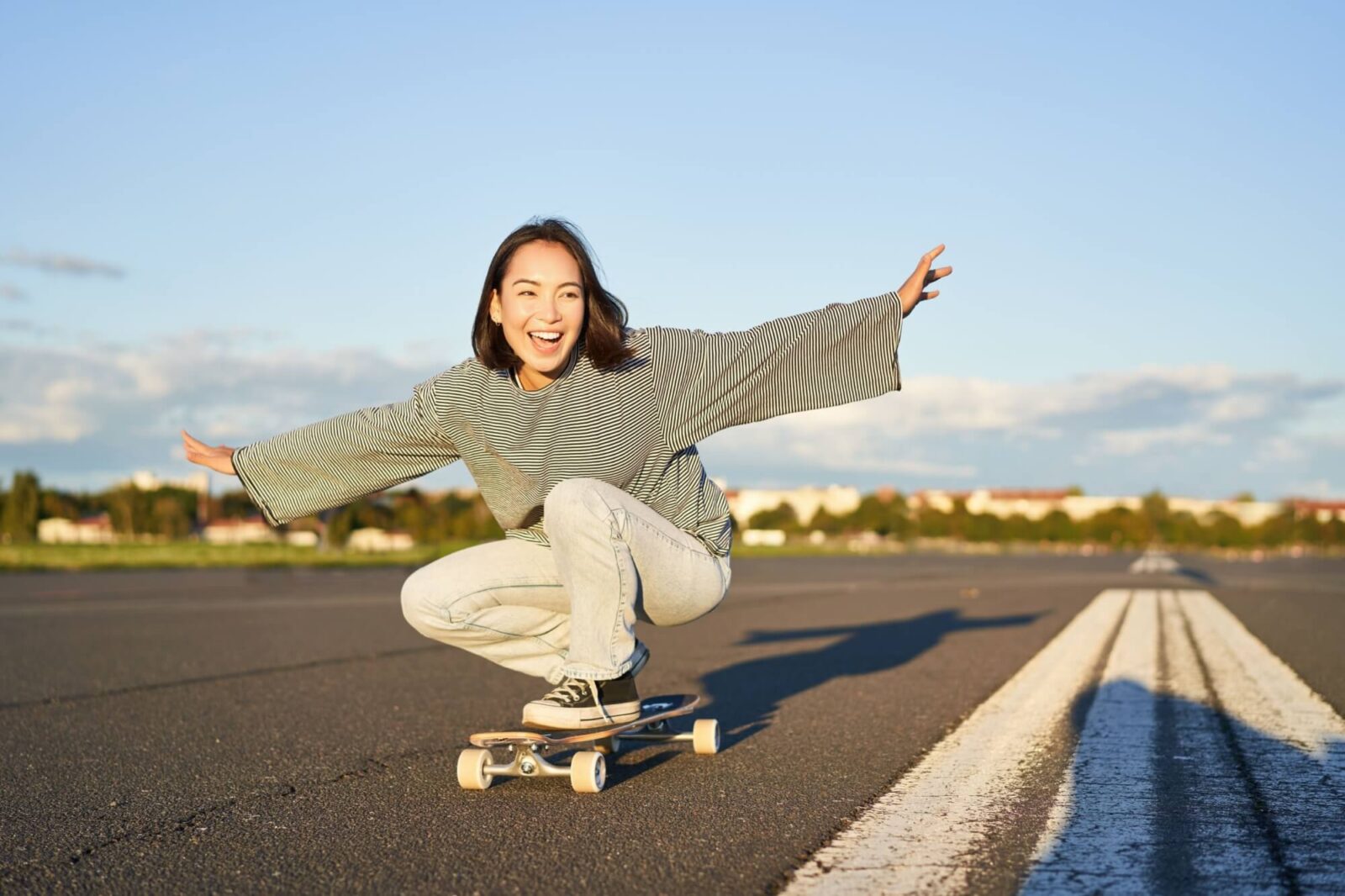 Happy girl riding her longboard on an empty sunny road