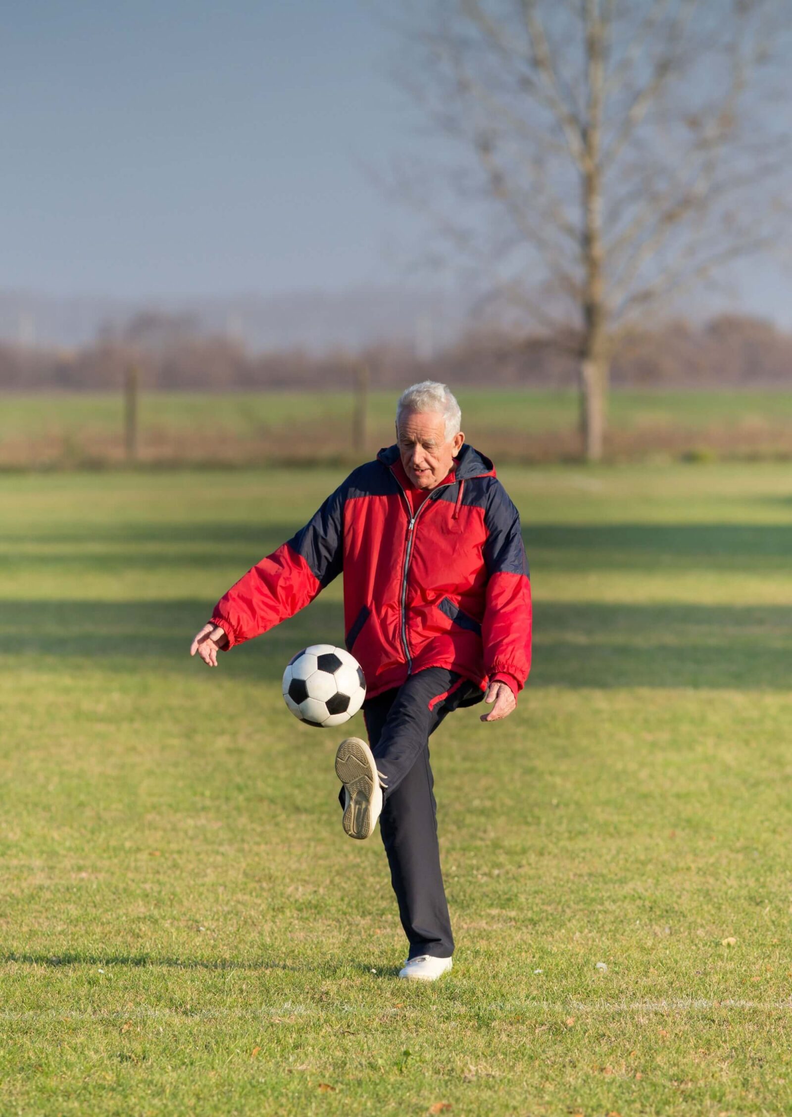 Old man kicking a soccer ball on the grass field