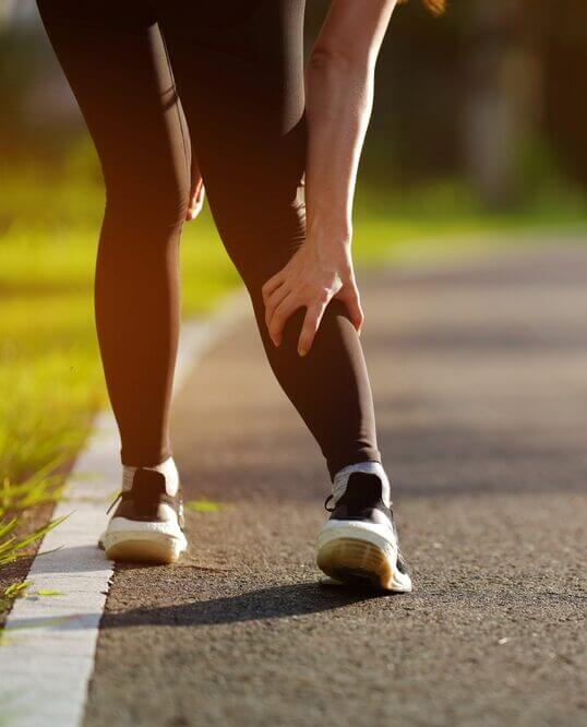 Sporty woman holding injured legs in the park