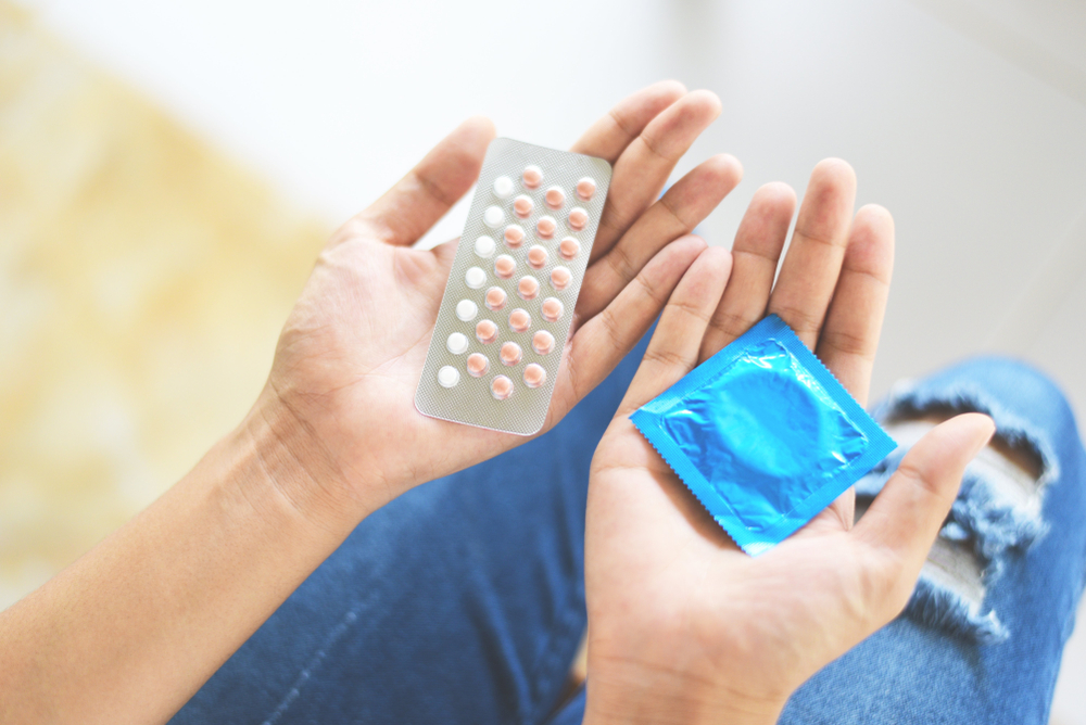 Woman holding contraception pills and condom in hand / Birth control contraceptive means prevent pregnancy or sexually transmitted disease
