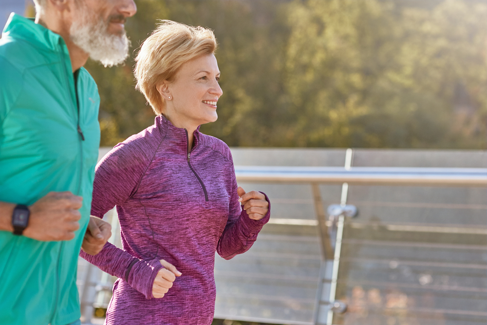 In motion. Cheerful active mature woman in sportswear smiling while running on a sunny day