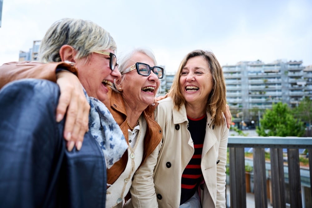 Group of three mature caucasian women enjoying embracing walk together laughing outdoor