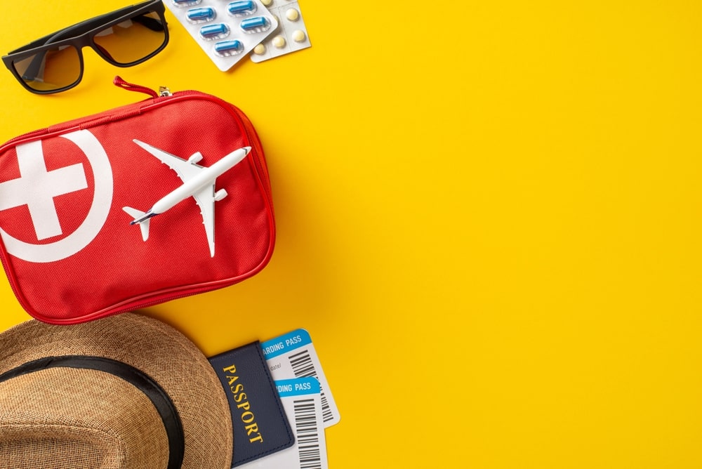 Travel safety essentials arranged with a red first aid kit, airplane, and passport against a vibrant yellow backdrop