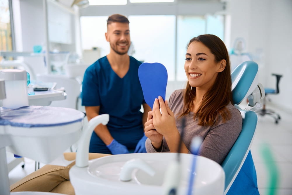 Happy woman looking her teeth in a mirror at dentist's office.