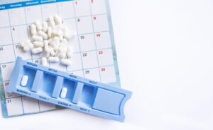 Dosing of pills by days, many pills are on the calendar and in the pillbox, organizer for pills on a white background with copy space.