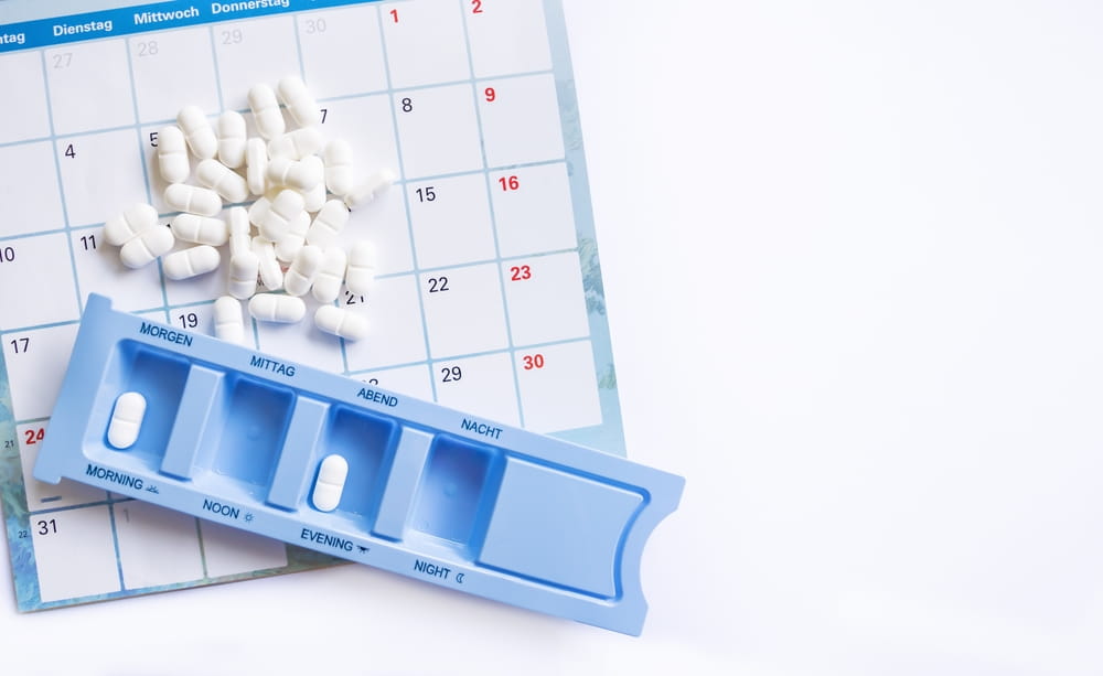 Dosing of pills by days, many pills are on the calendar and in the pillbox, organizer for pills on a white background with copy space.