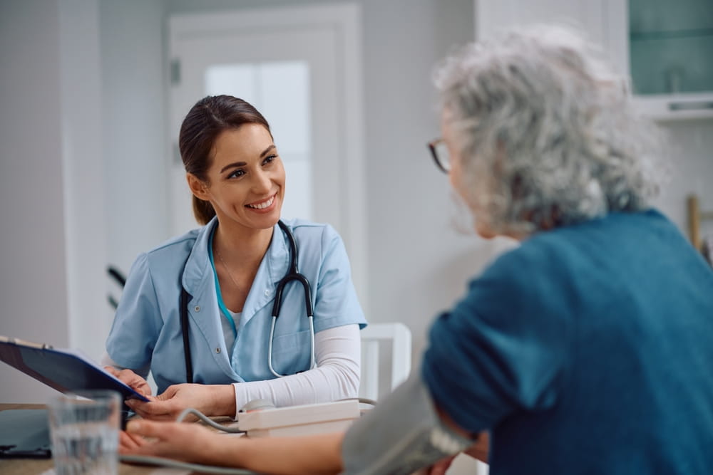 Happy visiting nurse communicating with senior woman at home.