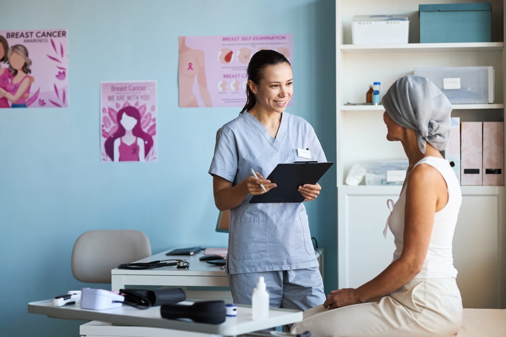 Young adult Caucasian female nurse smiling while holding clipboard and talking with middle aged Caucasian woman