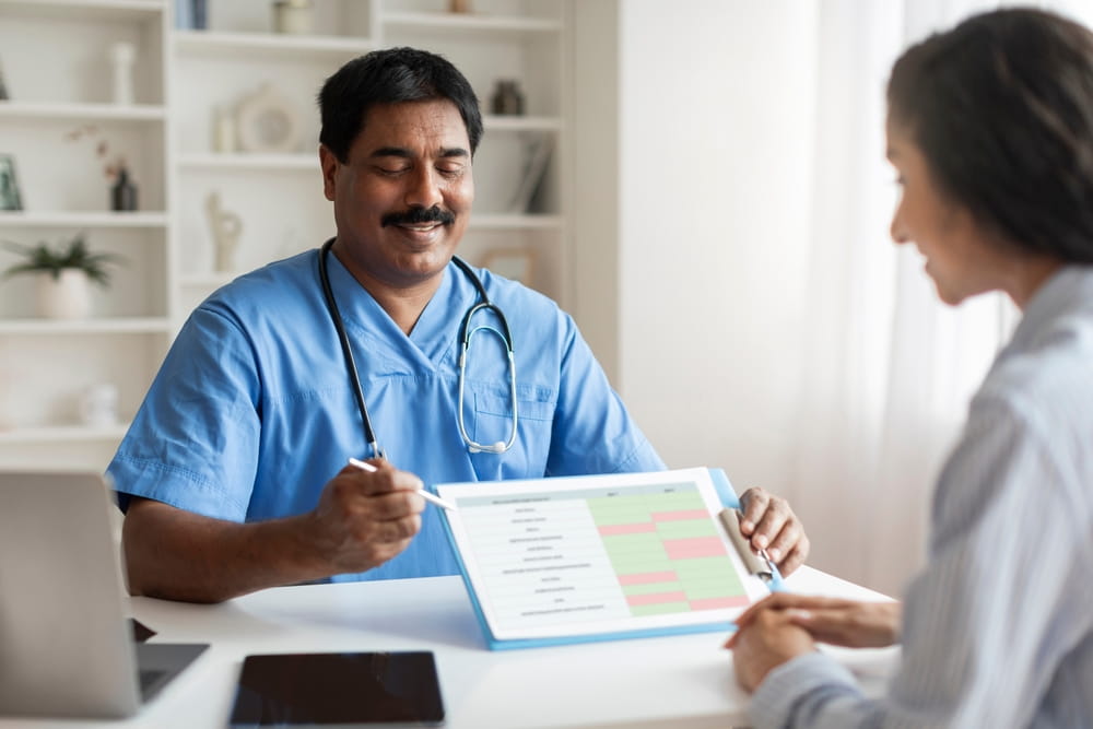 Indian Doctor Man Discussing Medical Test Results With Young Female Patient In Clinic