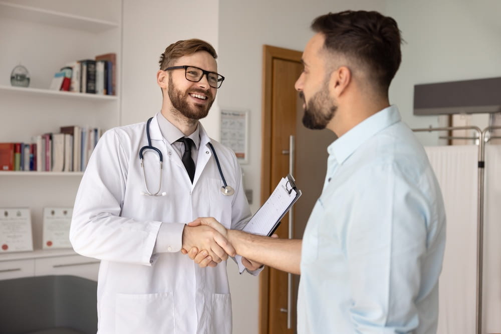 Successful doctor and patient interaction. Positive friendly young physician share firm handshake with male visitor