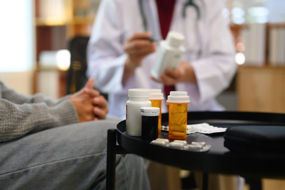 Close up view of several prescription medication bottles and pills on a table during a medical consultation.