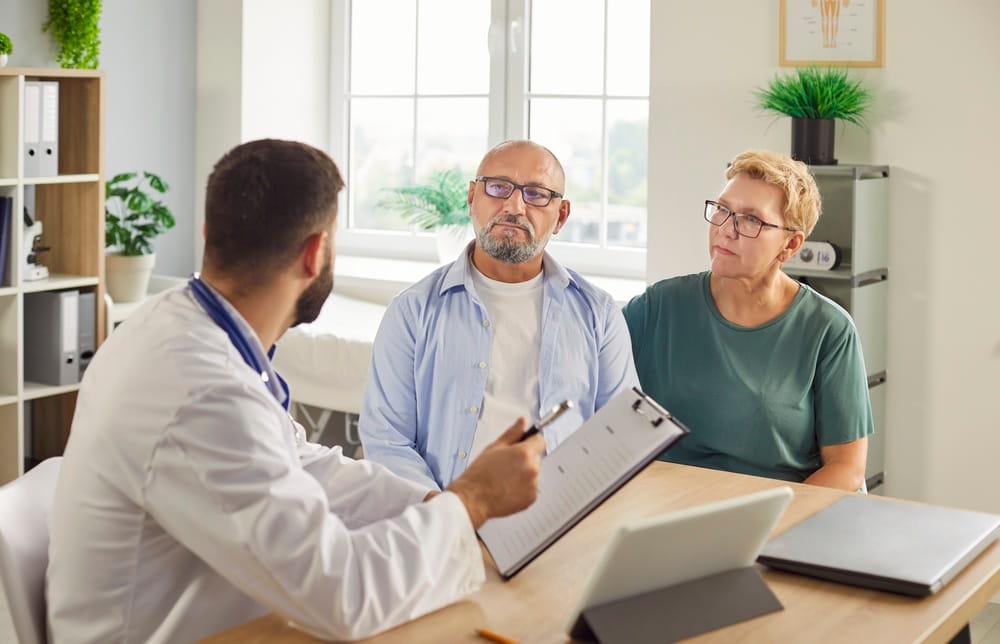 Doctor discusses treatment and care plans, reviews records and schedules followup with g senior couple in clinic consultation