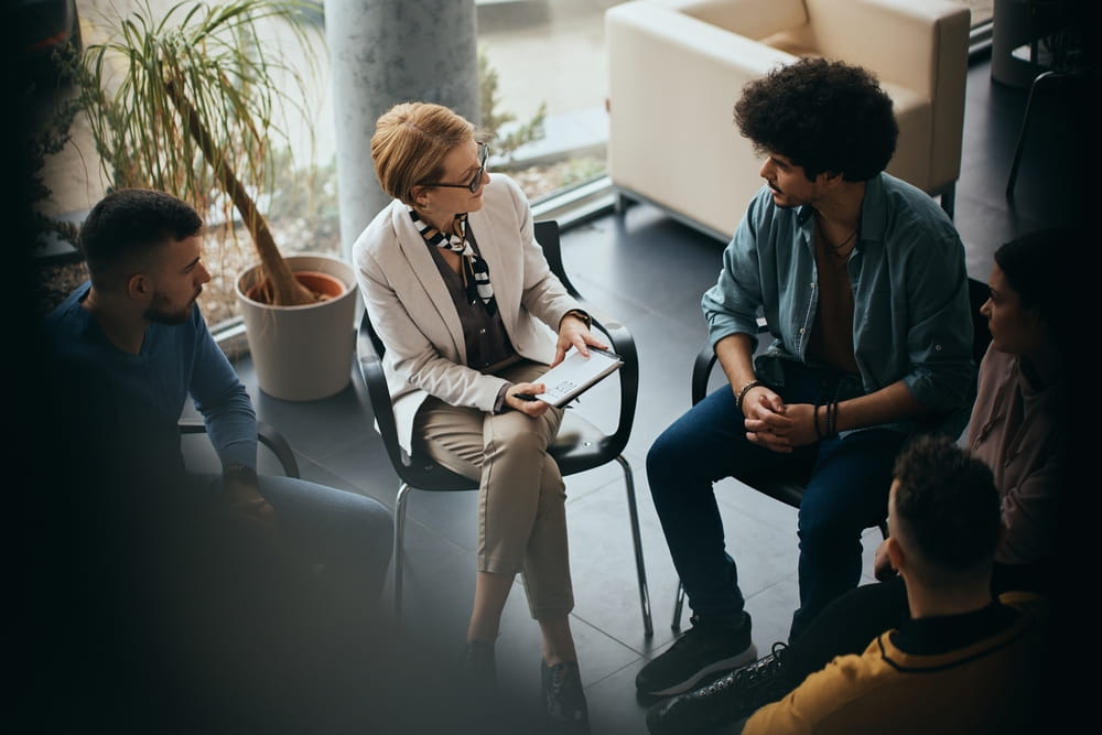 High angle view of mental health professional talking to participants of group therapy at community center.