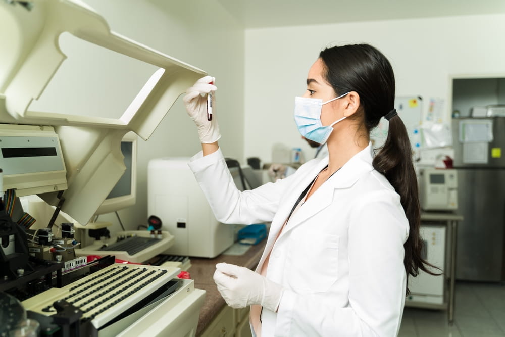 Young chemistry assistant with a face mask using a blood sample and making a laboratory test for a medical diagnosis