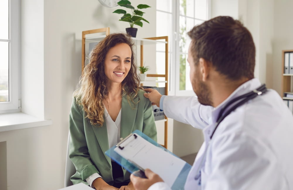 Portrait of a male doctor support young smiling female patient putting hand on her shoulder.