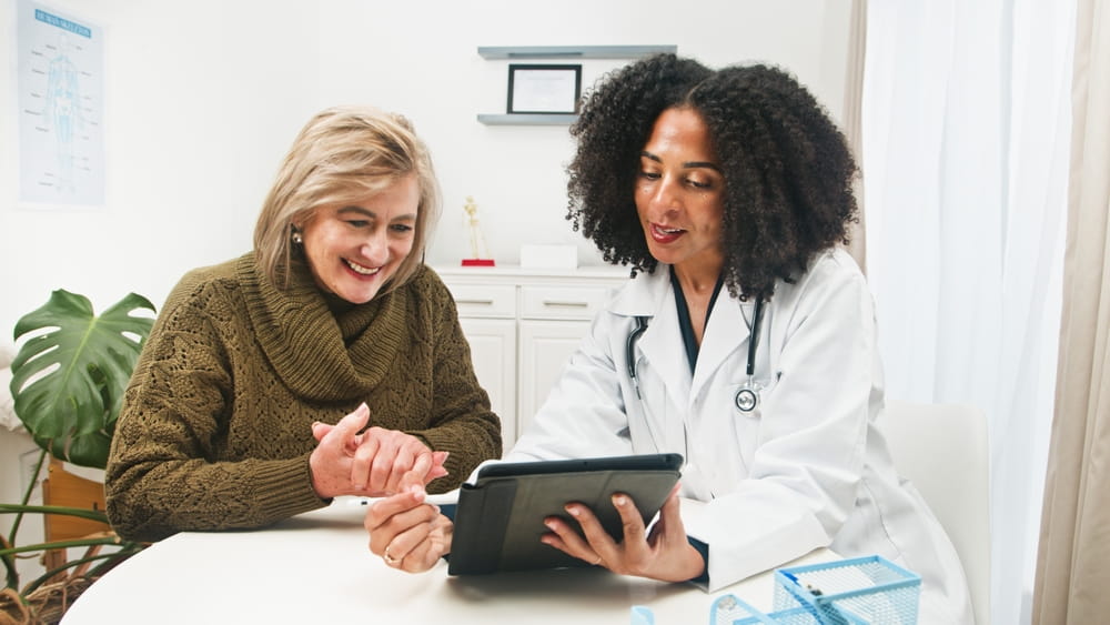 Doctor Shows Tablet To Happy Patient At Clinic During Friendly Medical Consultation