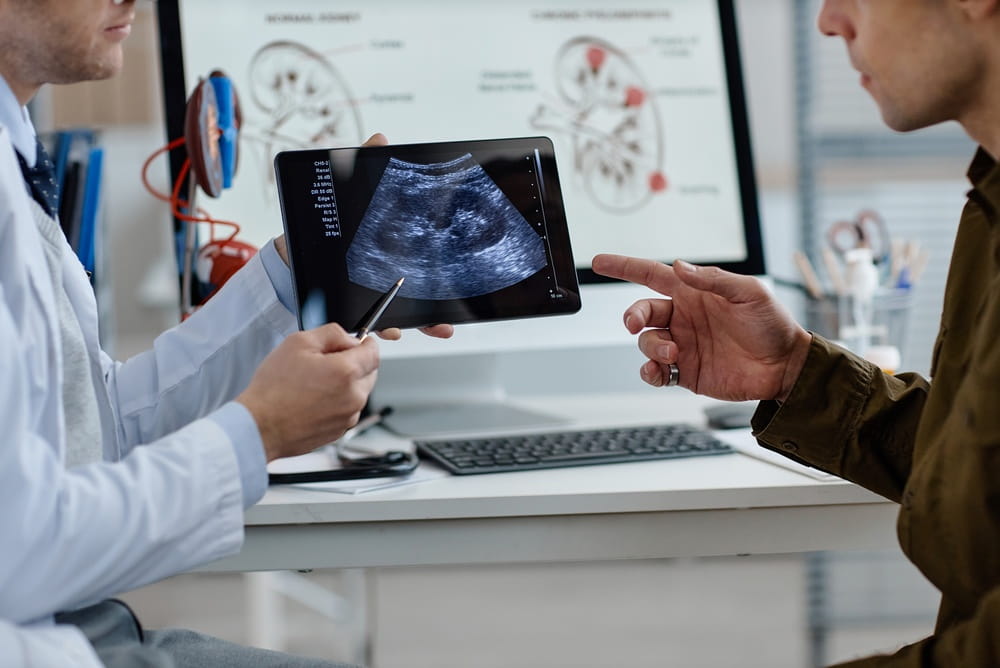 Middle aged Caucasian male urologist showing ultrasound scan on digital tablet to man during medical consultation in clinical office