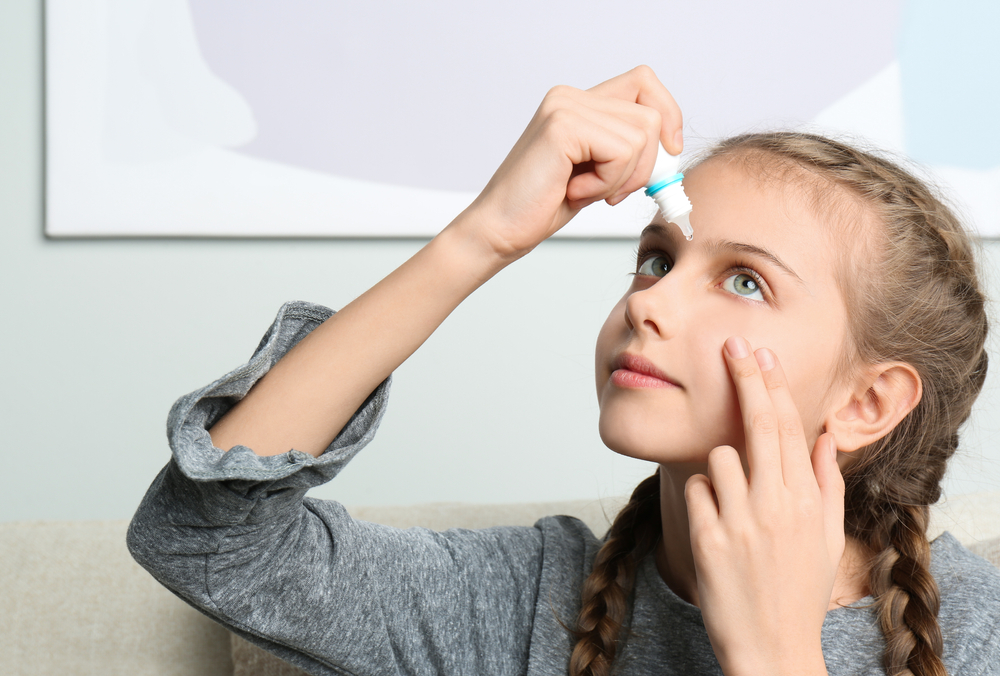 Adorable little girl using eye drops