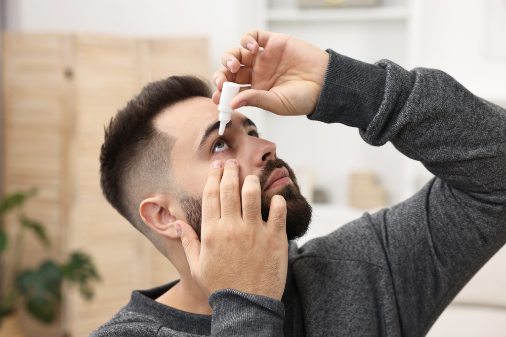 Young man applying medical eye drops