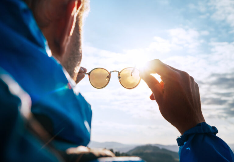 Backpacker man looking at bright sun through polarized sunglasses enjoying mountain landscape. Eye Vision Care human health concept image.