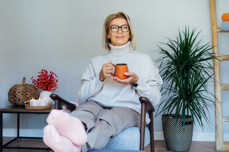 Middle aged woman relaxing with cup of hot drink in scandy style hygge interior home