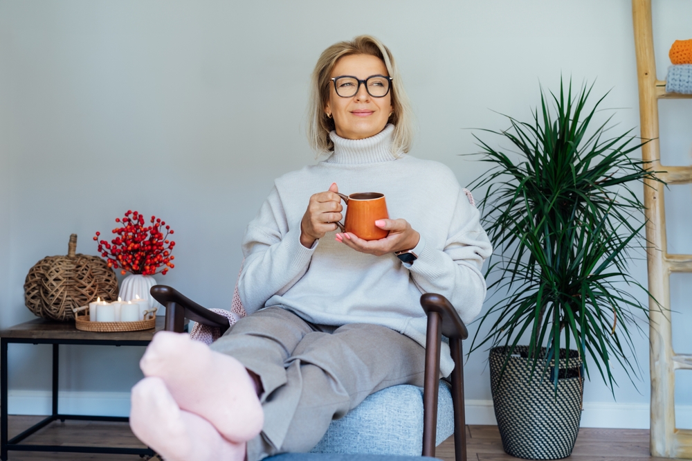 Middle aged woman relaxing with cup of hot drink in scandy style hygge interior home