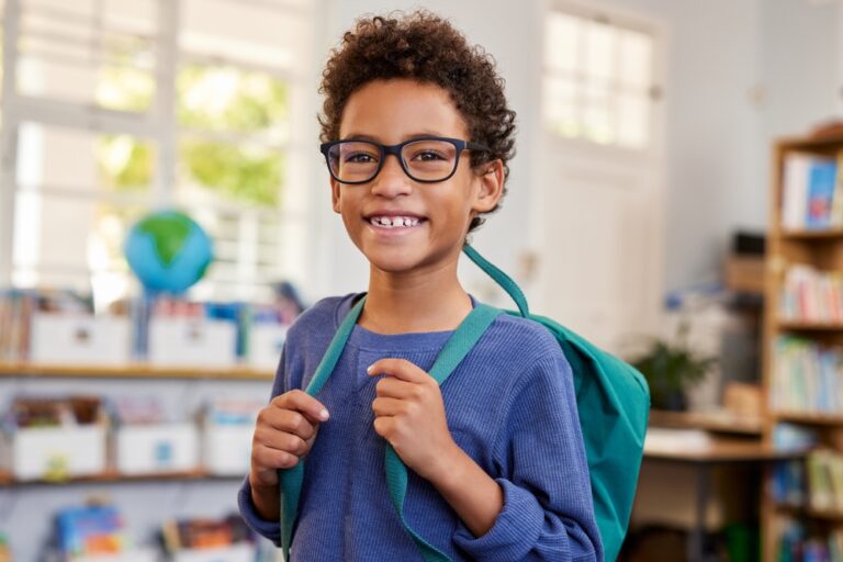 Portrait of smiling mixed race schoolboy wearing eyeglasses while looking at camera at primary school