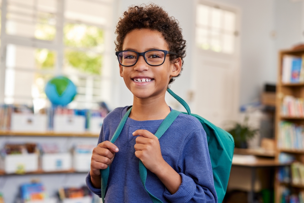 Portrait of smiling mixed race schoolboy wearing eyeglasses while looking at camera at primary school